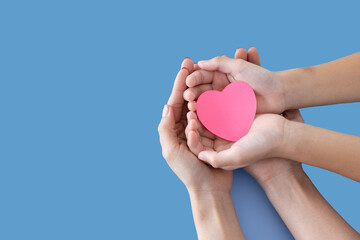 Heart in baby and mother hands isolated on blue background..Young woman and child holding heart in...