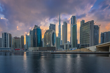 Obraz na płótnie Canvas Mystical sunset with a cloudy sky over the skyline of the financial district in Dubai. Business center with office buildings and skyscrapers around Burj Khalifa. Street with a bridge over the harbor