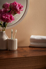 A small corner bathroom interior with round mirror, cotton towel, toothbrush and vase with beautiful pink flowers. Scene for advertising and branding product with blank space to place your design.