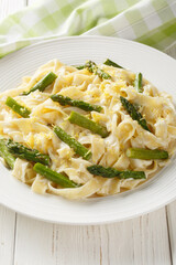 Fettuccine pasta with asparagus, lemon in a creamy cheese sauce close-up in a plate on the table. Vertical