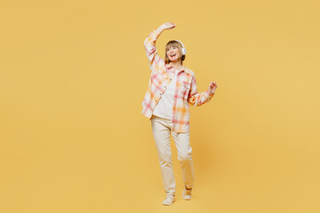 Full body elderly cheerful blonde woman 50s years old she wears casual clothes headphones listen to music raise up hadns dance isolated on plain yellow background studio portrait. Lifestyle concept.