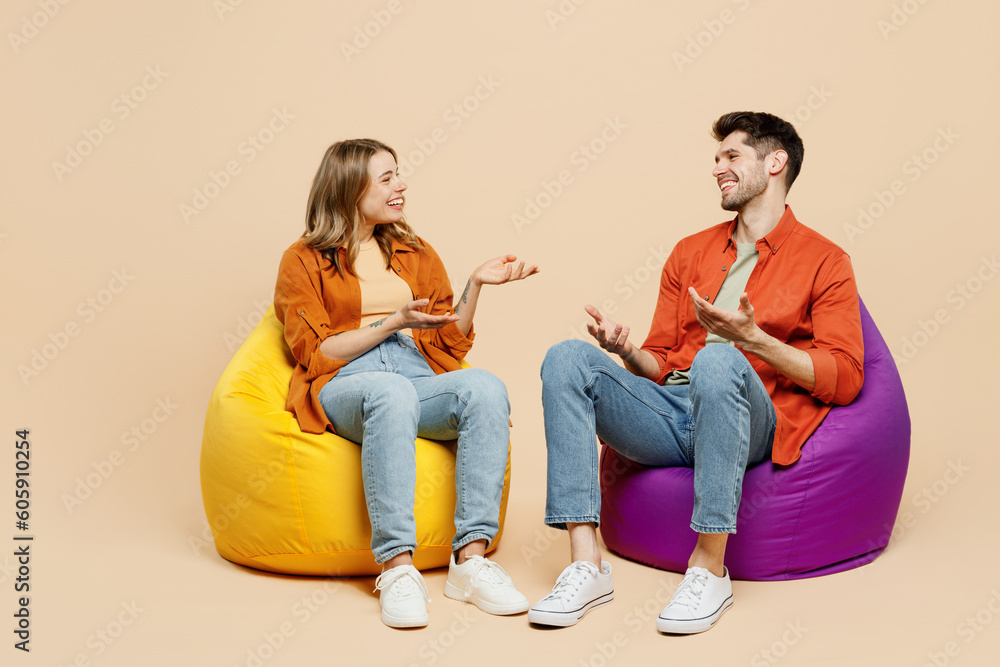 Poster Full body smiling young couple two friends family man woman wear casual clothes together sit in bag chair talk speak spread hands isolated on pastel plain light beige color background studio portrait.