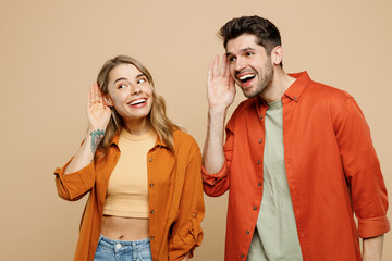 Young curious nosy couple two friends family man woman wear casual clothes try to hear you overhear listening intently together isolated on pastel plain light beige color background studio portrait.