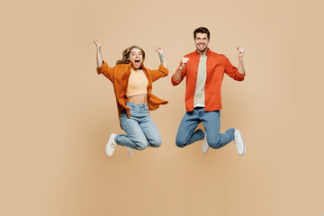Full body overjoyed excited fun happy young couple two friend family man woman wear casual clothes together jump high do winner gesture isolated on pastel plain beige color background studio portrait