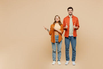 Full body young couple two friend family man woman wear casual clothes together point index finger aside on workspace area mock up show thumb up isolated on pastel plain beige color background studio