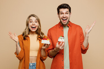Young couple two friends family man woman wear casual clothes looking camera together hold in hand eat piece of cake spread ahnds isolated on pastel plain light beige color background studio portrait.