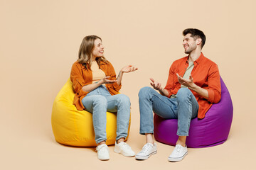 Full body smiling young couple two friends family man woman wear casual clothes together sit in bag chair talk speak spread hands isolated on pastel plain light beige color background studio portrait. - obrazy, fototapety, plakaty