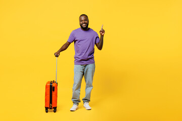 Traveler man wears casual clothes t-shirt hold suitcase point finger overhead isolated on plain yellow background Tourist travel abroad in free spare time rest getaway Air flight trip journey concept