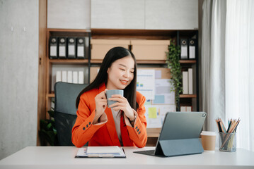Confident Asian woman with a smile standing holding notepad and tablet at the office.