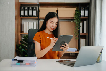 Young attractive Asian woman smiling thinking planning writing in notebook, tablet and laptop working from home, at office