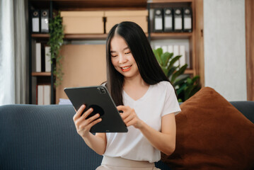 Fototapeta premium Asian woman using the smartphone and tablet on the sofa at home.