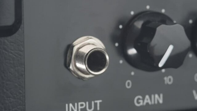 Somebody plugs instrument cable into a guitar amplifier. Connecting the jack bass to the bass amplifier. Close up. 