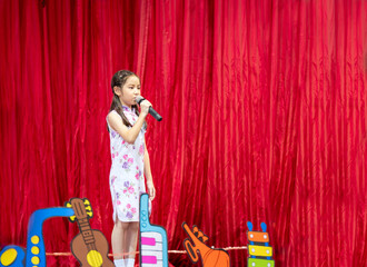 The Asian kid girl sing a song on stage at her school activity day, dress in Qipao style, red...