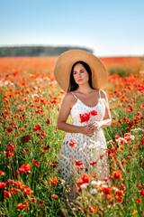 brunette woman in a field with poppies and daisies . She's wearing a big straw hat and a white lace dress