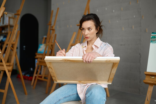 Attractive young woman artist holding canvas in hand drawing picture
