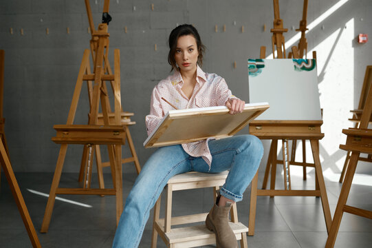 Beautiful casual woman artist drawing on canvas easel at professional art studio