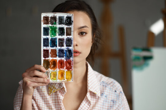 Portrait of young woman artist covering face with watercolor paints