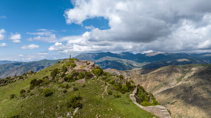 an ancient fortress on the top of a ridge in the mountains of Armenia against the backdrop of a forest and clouds on a May day taken from a drone