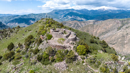 Fototapeta na wymiar an ancient fortress on the top of a ridge in the mountains of Armenia against the backdrop of a forest and clouds on a May day taken from a drone