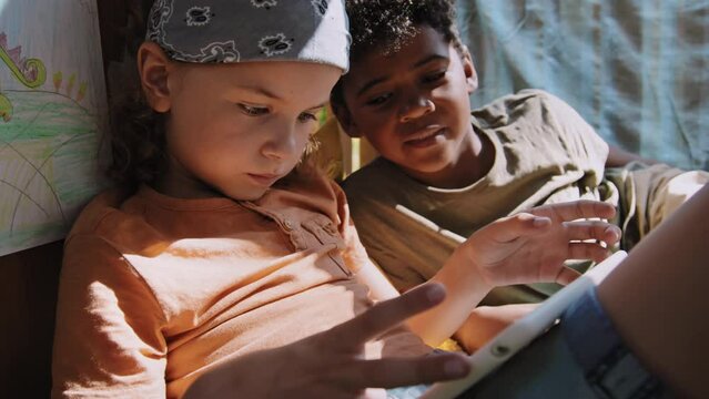 Slowmo medium shot of two African American and Caucasian elementary age kids playing games in tablet in treehouse at daytime