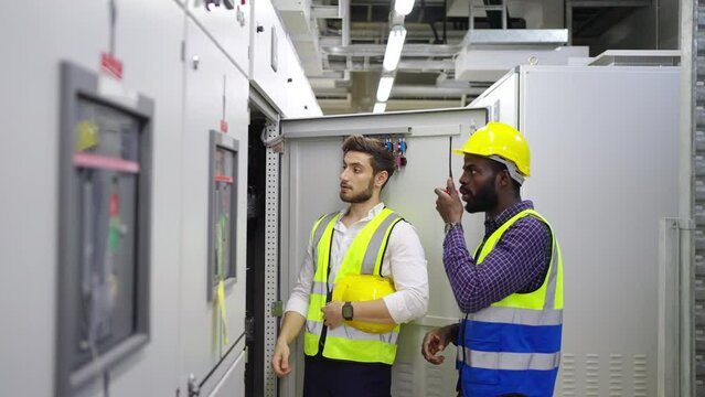 Professional electrical engineer in safety uniform working at factory server electric control panel room. Industrial technician worker maintenance checking power system at manufacturing plant room.