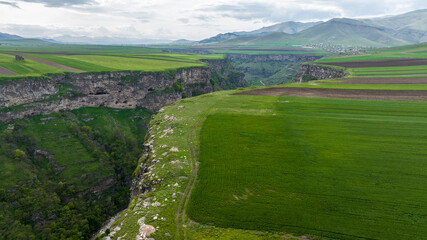 Fototapeta na wymiar panoramic view of the gorge with a river and green fields on a plateau against the backdrop of the mountains of Armenia view from a drone