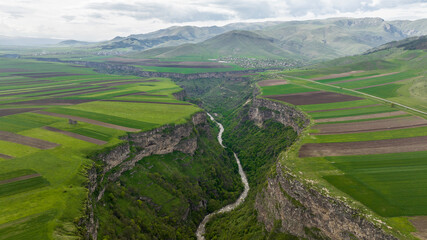 panoramic view of the gorge with a river and green fields on a plateau against the backdrop of the mountains of Armenia view from a drone