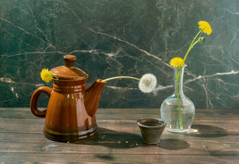 Still life with yellow dandelions in a teapot and a clear glass vase and a white dandelion and an antique lamp on a dark marble background. Conceptual laboratory of life.