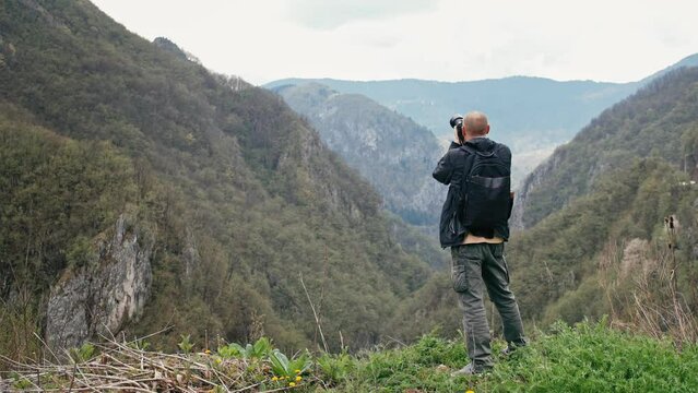 An adult Caucasian professional photographer taking pictures with a digital camera while hiking in the mountains. 