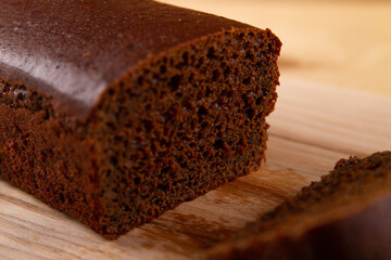 Dark bread displayed in  loaf and cut pieces, against light beige wooden backdrop. selective focus