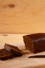 Light beige wooden base highlighting loaf and slices of dark bread. selective focus