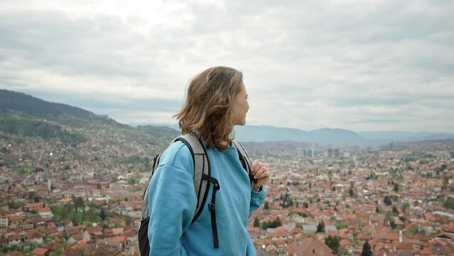 A young Caucasian woman with a backpack enjoying a beautiful top view of the city of Sarajevo