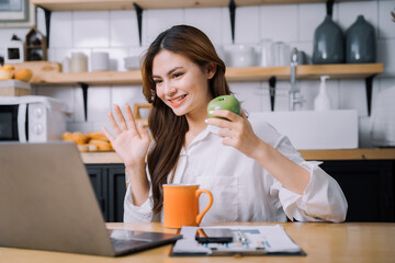 Pretty woman enjoying eating fruit while relaxing with laptop in kitchen Work from home.