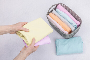 Women's hands fold clean clothes. Vertical storage of clothing in the baskets. Closet cleaning