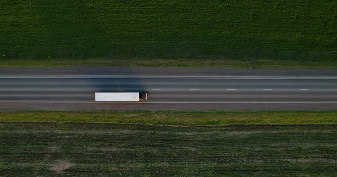 A truck with a semi-trailer is driving along a straight highway, aerial view. Truck traffic on the freeway, top view. Cargo transport.