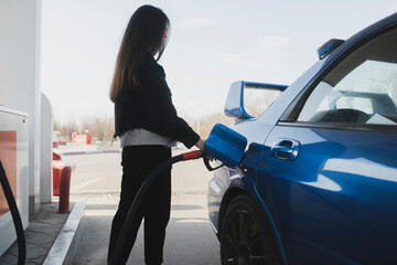 young girl is refueling the blue car on a gas station
