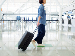 空港のロビーでスーツケースを持って歩く女性