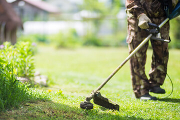 Man mowing tall grass with electric or petrol lawn trimmer in backyard. Gardening care tools and equipment. Process of lawn trimming with hand mower