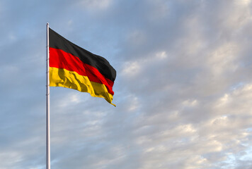 Waving German flag against a blue sky with clouds and empty space for text. Room for text.