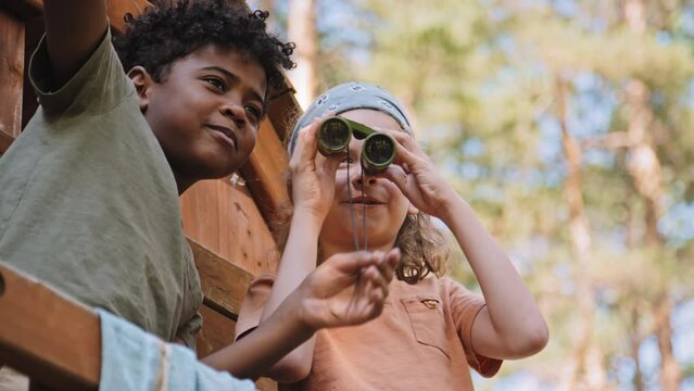 Low angle of African American and Caucasian elementary age boys playing forest rangers pretend game in treehouse at daytime