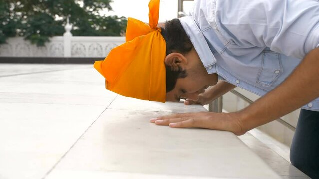 Closeup shot of a boy wearing an orange head scarf bowing down and touching his head on the floor for prayers at the Gurudwara . A young man in casual clothes is offering his prayers at a Gurdwara ...