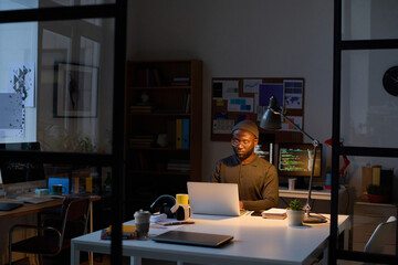 African American programmer working on computer at his workplace in office till late night