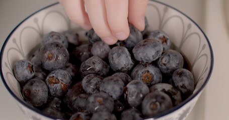 Close-up of blueberries in a plate. Children's hand takes a black fruit. The use of fresh berries in the complementary diet. Source of vitamins and minerals. Natural fruit juice.