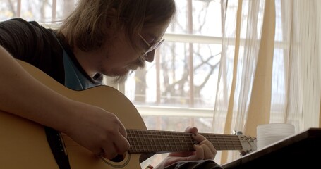 Mental exercise in free time. Make a melody. He puts chords by hand, creating music. Glasses eyes. Painted nails male musician plays guitar room near the window gratings opening frames. 