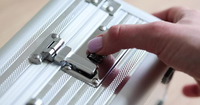 Female hand opens silver briefcase using combination lock. Young woman with neat manicure unlocks metal case on wooden table in office
