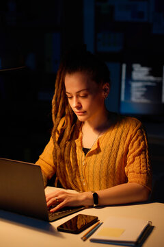 Vertical image of young programmer doing online project on laptop till late night in office