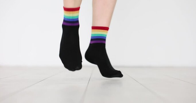 Stepping feet dressed in black socks with image of rainbow flag. Clothes with LGBTQ flag decor on white background. Support for vulnerable social groups