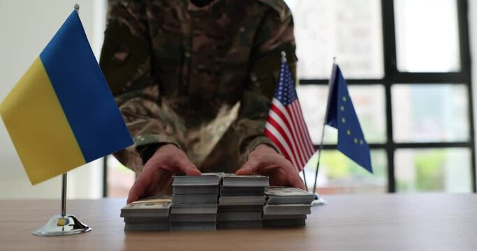 Military officer moves stacks of dollar banknotes on board table with international flags in audience. Financial support and help for Ukrainian soldiers slow motion