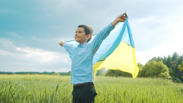 boy with Ukrainian flag in the wheat field. Little kid waving national flag praying for peace. Happy child celebrating Independence Day.