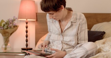 Woman attention focus on bed, using tablet in hands, home wifi network. Using a mobile application to check notifications online.